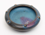 PEQUENA TIJELA lava-pinceis para mesa de letrado, emporcelana chinesa com coberta monocromática celadon azul do tipo Jun com mancha escorrida em tons magenta. Bojo circular achatado, com bordarealçada por pequenas tachas em relevo e base retraída. Peça de coleção. Dinastia Song (960-1279). Med. 2.5cm X 8.0 cm X 8.0 cm