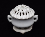 COLECIONISMO - RARO INCENSÓRIO chinês com base e tampa em porcelana Blanc de Chine. Recipiente liso de formato globular achatado, ladeado por alças estilizadas. Tampa circular abobadada e vazada, moldada com gomos e encimada por pequena pega. Base triangular, lavrada em relevo com folhas de lótus, apoiada em três pequenos pés curtos. Séc. XVIII. Peça de coleção. Med. Alt. 17,0 cm  Diâm. 12,5 cm.