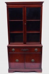 BASSETTE FURNITURE INDUSTRIES, INC. - Armário louceiro americano estilo inglês construído em madeira nobre e folheado. Armário reto, apresentando 1 gaveta com aplique entalhado em forma de feixe de trigo na parte central e alinhada sobre par de portas com prateleira interna. Alçada com frente envidraçada com 2 prateleiras internas e, realçada por molduras e encimada por frontão reto. Ilhargas lisas e saia retilínea, apoiada em pés retos. Marca da Manufatura selada dentro da gaveta e na parte de trás numerada. OBS:  Pequena Perda de folheado nos pés frontais. Marcas de uso. Med. Alt. 1,77  m Larg. 0,92 m e Prof. 0,43 m.  INFORMAÇÂO ILUSTRATIVA: Bassett Furniture Industries, Inc. é uma fabricante e varejista de móveis com sede em Bassett, Virgínia, Estados Unidos. Foi fundada em 1902 por John D. Bassett, Charles C. Bassett, Samuel H. Bassett, Reed L. Stone. Bassett Furniture é um dos fabricantes de móveis mais antigos da Virgínia