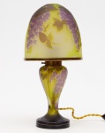 LUMINÁRIA DE MESA Champignon estilo Art Nouveau, em pasta de vidro ornamentada por glicínias em tons roxos e folhagens verdes sobre fundo amarelo. Montagem com armação em bronze. Haste no formato de balaústre apoiado em base circular esparramada, sustentando cúpula abobadada. OBS: Sem assinatura. Med. Alt. 30 ,0 cm