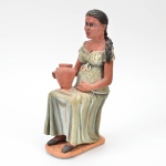 Clesiana Ribeiro - Escultura em barro policromado, assinada, e datada 10/2003, retrata figura de Mulher sentada com jarro no colo, altura 26 cm.
