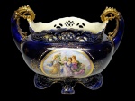 ROYAL VIENNA - Magnifica floreira palaciana em rara porcelana finamente decorada com linda cena representando as três Graças. Borda com rico trabalho fenestrado, fundo com requintado acabamento em azul cobalto com riquíssimos filetes, pintura e cobertura a ouro. Marca da preciosa manufatura Royal Vienna sobre a base. Tchecoslováquia final do séc XIX. Excelente estado de conservação. Mede aprox 23 x 31 x 16 cm.