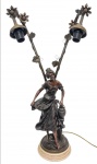 Elegante luminária dupla, executada em petit bronze de ótima fundição, representando expressiva figura feminina e ricos motivos florais. Sustentada em base de resina semelhante ao mármore. Perfeito estado de conservação, mede 63,5 cm de altura x 16,0 cm de diâmetro da base.