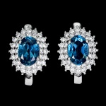 Clássico e elegante par de brincos em prata de lei espessurada a ouro branco, design exclusivo de excepcional ourivesaria com belíssimo Topázio London blue de 7.0 x 5.0 mm, clássica lapidação oval brilhante, adornado por rico trabalho, fino acabamento e majestosas coroas de Zirconias extra brancas de lapidação brilhante. Perfeito estado de conservação, sem uso. Medem 1,2 x 1,0 cm. Origem África.