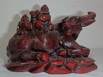 Escultura em resina vermelha representando figuras orientais montadas em um touro. Comprimento 12,5 cm