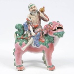 Escultura em porcelana chinesa do Séc. XIX, reproduz figura de Divindade, montada em um Qilin, ricamente policromado, altura 27 cm. Apresenta pequena falta de material na ponta da saca nas costas da figura, vide foto extra em detalhe.