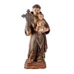 Portugal Séc. XIX - Monumental Imagem de Santo Antônio Crucífero, esculpida à mão, com a mão esquerda carrega o livro dos ensinamentos, sustentando o Menino Jesus e com a mão direita segura uma Cruz em prata de lei. Vestido com hábito comprido da sua ordem, cingido á cintura por cordão de ponta pendente com três nós, símbolos dos votos da pobreza, castidade e obediência, indumentária de dobras turgidas, ricamente decorada a ouro sobre fundo castanho com padrão geométrico, encimado por estrelas estilizadas com término em faixa a ouro com enrolamentos vegetalistas e volutas. O Menino Jesus, vestido com roupa de seda em tons de bege, com a mão direita em sinal de benção. A base em madeira recortada, facetada e moldurada em dégradé, decorada com marmorizados em vários tons, altura total 53 cm.