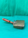 Antigo mordomo silencioso, feito de bronze com um cabo de madeira. Este utensílio era usado para recolher migalhas de mesa de forma discreta durante as refeições. O design inclui uma tampa articulada que se abre para recolher as migalhas e depois se fecha para evitar que caiam. O cabo de madeira proporciona uma pega confortável e isolante. Abafadores de migalhas como este eram comuns em épocas passadas, refletindo a etiqueta e os costumes da época.Como se encontra nas fotos medindo 29 cm de comprimento. 
