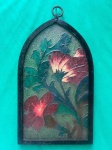 vitral em forma de arco ogival, emoldurado por metal. O vitral representa flores em tons de vermelho, rosa e verde. O estilo das flores é um tanto estilizado, com linhas marcadas e cores vibrantes. Como se encontra nas fotos medindo 41 cm de altura.