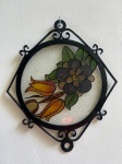vitral circular emoldurado por uma estrutura de metal preta com detalhes ornamentais. O vitral exibe um design floral estilizado com uma flor grande.Como se encontra nas fotos medindo 32 cm X 31 cm.  