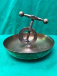 quebra-nozes de metal antigo, com um design que inclui uma base em forma de tigela e um mecanismo de quebra em forma de anel com uma manivela em T. como se encontra nas fotos.  