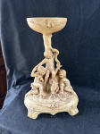 Vintage, centro de mesa vintage antigo, feito em polímero com um tom creme, apresentando três querubins (cupidos ou putti). A peça serve como suporte para um recipiente superior. A base é adornada com detalhes ornamentais, e toda a escultura exibe um estilo clássico e elegante.Como se encontra nas fotos medindo 34 cm de altura por 24 cm de largura na base.