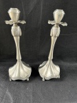 Vintage, belo par de castiçais, em metal espessurado a prata. Eles apresentam um design elegante e ornamentado, estilo art deco,  com uma base larga e ondulada que se estreita em um corpo curvo e decorado com detalhes florais e outros motivos. O suporte para a vela em si tem um formato que lembra um botão de flor. Como se encontram nas fotos medindo 35cm de altura.