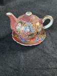 BETSONSMiniatura de um bule de chá Kutani Moriage Dragonware, que é um tipo de cerâmica japonesa conhecida por seus detalhes intrincados e cores vibrantes feito a mão. A decoração apresenta figuras humanas pintadas à mão, típicas da arte Kutani, e um design Moriage, que se refere às aplicações em relevo na superfície da peça.Como se encontra nas fotos. 