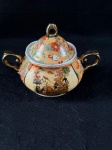 SatsumaAçucareiro de fina porcelana Satsuma, fina porcelana japonesa conhecida por seus detalhes intrincados e cores vibrantes. Datado da década de 1940, durante o período da ocupação do Japão, apresenta uma cena detalhada de gueixas e figuras da nobreza, com trabalhos finos e incrustações, além de detalhes pintados à mão. A cerâmica Satsuma. São considerados peças de colecionador. Como se encontra nas fotos.