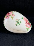 Belíssimo porta-joias vintage, em formato de ovo, decorado com motivos florais. As flores são predominantemente rosas, em tons de rosa claro e escuro, com detalhes em verde nas folhas. O fundo do porta-joias é branco.Como se encontra nas fotos medindo 18 cm de comprimento.  
