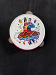 pandeiro de brinquedo vintage de metal com litografia. Ele apresenta um casal dançando salsa no centro, rodeado por confetes e notas musicais coloridas. O pandeiro é feito de metal e possui pequenos címbalos nas laterais. Pandeiros como este eram populares como brinquedos na década de 1950 e 1960. Como se encontra nas fotos medindo 16 cm de diâmetro. 