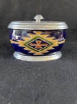 Vintage compoteira dinamarquesa em fina maiolica. Apresenta uma decoração em azul com desenhos geométricos em tons de amarelo, verde e marrom. A tampa é de metal prateado, assim como a base do pote. Conforme nas fotos medindo 18 cm por 11 cm.   