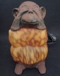 Antiga luminária representando macaco  que  Não  Vê , sendo cabeça e pés em ferro fundido e  o. corpo em pasta de vidro , na cor âmbar . Partes de ferro apresentam  desgastes. Medindo : 22 x 10 x 12 cm .