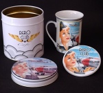 Bela caneca colecionável em porcelana pintada e esmaltada com alusão a aviação, figura de aeromoça loura dos anos 50 e de aviões, no interior da caneca tem um avião;  acompanha suporte para a caneca do mesmo material também com a mesma estampa e uma lata. Medindo a caneca 9 cm de altura e a lata com 11 cm de altura.