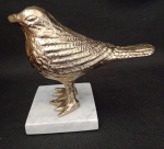 Pássaro  em cerâmica metalizada trabalhado em relevo na cor ouro com a base em mármore na cor branca . Medindo 11 cm de altura X 21 cm de comprimento com o rabo do pássaro A base mede 8,5 X 7 X 1cm.