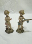 Par de enfeites na forma de querubins com instrumentos em resina. Medindo o maior 12cm de altura.