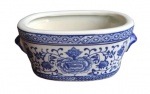 Bela floreira oriental em porcelana, na forma oval, ricamente policromada de azul e branco, exaltando florais e guirlandas. Medidas 25x15x10cm.