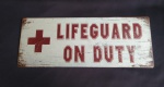 Placa decorativa em  metal com emborrachados de efeitos envelhecidos e dizeres "LIFEGUARD ON DUTY' . Medida 18x46cm.