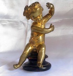 Escultura em bronze representando criança "Putti" apoiada sobre base de madeira torneada medindo a escultura 17 cm de altura.