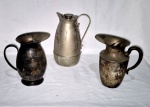 Três peças em metal espessurado a prata sendo uma refresqueira térmica com tampa com cortiça medindo 25 cm de altura, acompanha duas jarras necessitando limpeza e medindo 20 cm de altura uma delas marcada wollf.