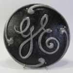 COLECIONISMO FERROVIÁRIO - Placa de identificação do fabricante de Locomotivas e vagões, com inscrição `GE` em alto-relevo. Logo da Fábrica General Electric. Reedição em Metal. Mede aprox. 21,8 cm de diâmetro.