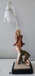 Gracioso abajur adornado por escultura em resina italiana representando Dama com carrinho de flores, sobre base quadrada. Funcionando, altura total 59 cm.