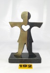 Escultura confeccionada em bronze de jovem com coração vazado ao meio, dividida em bronze dourado e patinado de preto (apresenta desgastes na patina preta), base em granito negro, medindo 17,5x12cm.