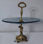 Elegante Centro de Mesa / Fruteira, em vidro grosso com lindos desenhos em relevo, bordas recortadas, na tonalidade azul claro, com haste de sustentação em bronze com querubin ricamente cinzelado, pés quadripoides em patas de leão e com rostos de anjos. Dimensões: 41 cm X 37 cm (Alt./Diâm.).