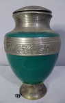 Urna com tampa,  em metal prateado, partes esmaltada verde. Ricamente decorada, em relevo, folhas e folhagens. Muito bem conservada. Medindo 27x18cm.