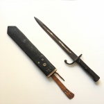 Antiga baioneta com lâmina em metal e cabo em madeira com avarias. Exemplar parte de coleção. Dimensões: 43 cm.