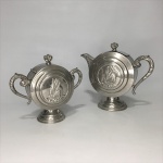 Antigo conjunto com BULE E AÇUCAREIRO em metal cinzelado , bojo circular ,decorado com figura de embarcação em alto relevo. Pega , alça e bico decorado com folhas de acanto. Dimensões:  Bule 17 cm x 19 cm e açucareiro 15 cm x 18 cm.