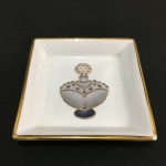 Antigo porta-cartões em porcelana esmaltada na cor branca, decorado com figura de perfumeiro, pintado à mão com borda pintada à ouro. Pequeno bicado na borda. Exemplar parte de coleção. Dimensões:13 cm x 13 cm.