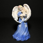 Bela e delicada sineta em fina porcelana esmaltada no formato de figura feminina com asas segurando cruz. Perfeito estado. Exemplar parte de coleção. Dimensões: 14 cm x 8 cm x 8 cm.