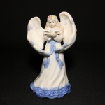 Bela e delicada sineta em fina porcelana esmaltada no formato de figura feminina com asas segurando pomba. Perfeito estado. Exemplar parte de coleção. Dimensões: 14 cm x 8 cm x 8 cm.