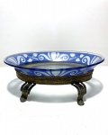 Delicada travessa em vidro no formato oval decorado com detalhes vegetalistas sobre faixa na cor azul com suporte de metal. Dimensões: 3 cm x 15 cm x 21 cm.