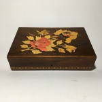 Antiga e bela caixa em madeira marchetada, formato retangular, decorada com faixa em tons claro e tampa com imagem de rosa e contorno do território brasileiro. Presença de arranhões e de desgaste. Não possui chave. Dimensões: 5,5 cm x 15 cm x 23 cm.