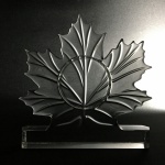 Bela folha de bordo canadense feita em bloco de cristal. Ao centro espaçocircular possivelmente para relógio. Dimensões: 15 cm x 15 cm x 3 cm.