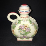 CERAM ARTE - Bela e antiga garrafa em porcelana com tampa . desenhos  em alto relevo florais e ao centro casal  se beijando , outro lado da garrafa desenhos em alto relevo  florais e ao centro arranjo floral. Dimensões: 15,5 cm x 12 cm.