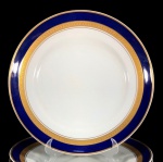 SCHMIDT - Elegante prato raso em fina porcelana esmaltada, decorada com faixas azul cobalto e faixas em alto relevo gravadas à Ouro 22k. 01 unidade. Dimensões: 25 cm diâmetro.