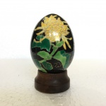 Belo ovo em porcelana decorado com flores sobre fundo preto pintados a mão. Realces filetados a ouro. Acompanha base em madeira. Dimensões: 9 cm x 5 cm.