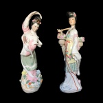 Duas esculturas orientais de figura feminina de porcelana. Uma escultura com parte faltando. Dimensões: 35 cm altura (maior peça).