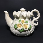 Antigo bule de porcelana decorado com arranjos florais em alto relevo. Dimensões: 11 cm.