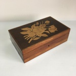 Caixa de madeira marchetada decorada com faixa geométrica nas laterais e arranjo floral na tampa em dois tons.. Sinais de desgastes. Dimensões: 7 cm x 14 cm x 22 cm aproximadamente.