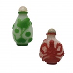 SNUFF BOTTLES - Dois recipientes de cristal de rocha, um na cor verde, decorado com ave e o outro na cor vermelho, decorado com figura em posição de meditação  Dimensões: 8 cm.